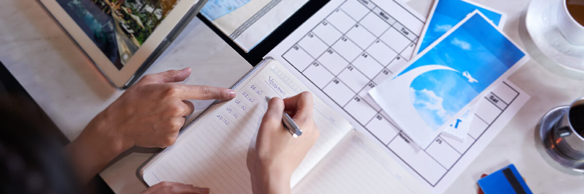 Two people crafting a travel itinerary; writing times and activities in notebook.